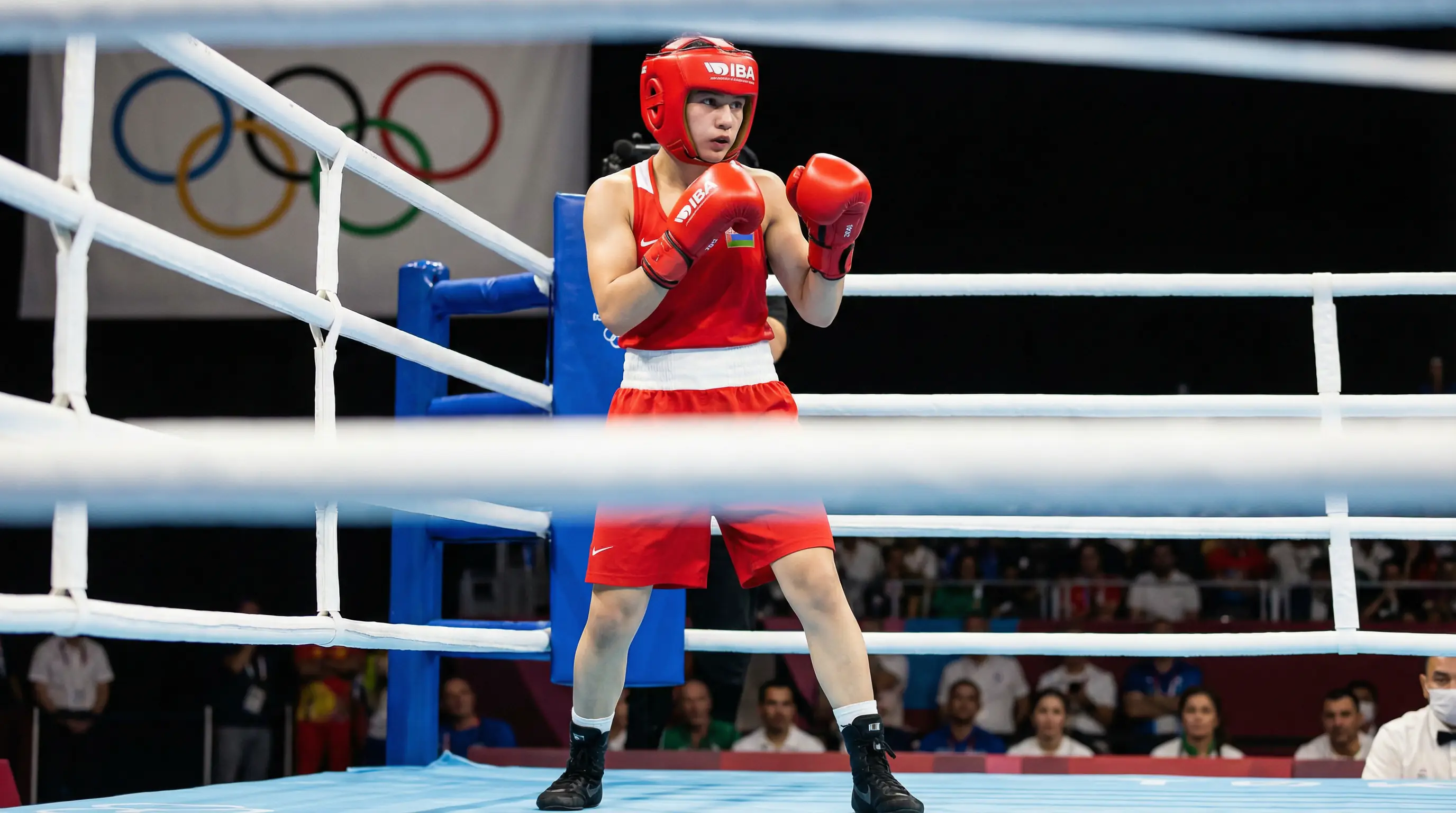 Amateurboxer mit Kopfschutz und olympischen Ringen im Hintergrund
